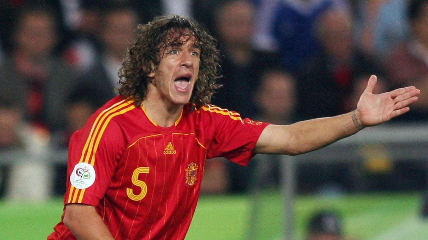 Hậu vệ Carles Puyol với mái tóc xù đặc trưng, thi đấu đầy quyết liệt trong màu áo Tây Ban Nha.